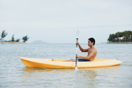 A Tropical Adventure: Happy Asian Man Kayaking on the Beach, Enjoying Summer Vacation
