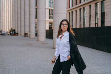 Confident businesswoman walking in urban environment, carrying blazer.