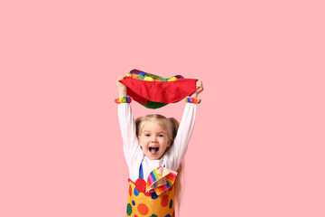 Cheerful little girl in clown costume with hat on pink background