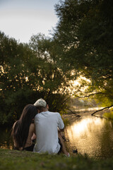 pareja de enamorados sentados a la orilla de un lago de espaldas a camara mirando el aterdecer a contraluz