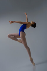 ballerina in a blue bodysuit and ballet shoes poses in a photo studio in motion showing beautiful...