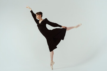 ballerina in a black dress and ballet shoes poses in a photo studio in motion showing beautiful...