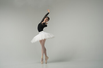 ballerina in a black bodysuit and tutu poses in motion showing ballet elements while standing on...