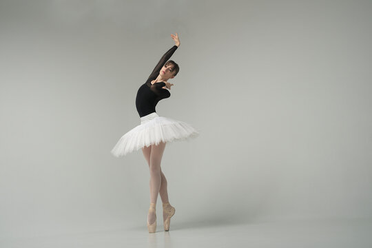 ballerina in a black bodysuit and tutu poses in motion showing ballet elements while standing on pointe shoes
