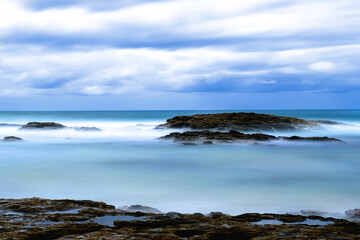 Dramatic landscape on long exposure to create silky water  view over  rock on sandy beach. Coastal feature.