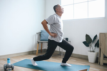 Elderly man stretching his leg, doing fitness exercises on mat at home 