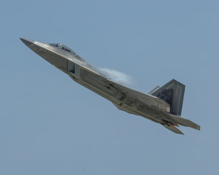 F-22 figher makes a climbing pass with vapor trail coming off the upper fuselage