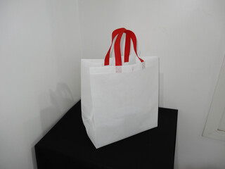 Beautiful Non Woven grocery shopping white bag with red handle loop isolated on black table against white wall background