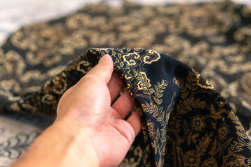 A hand holding traditional Indonesian fabric, namely batik cloth. Indonesia with elegant classic...