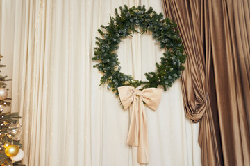 Christmas decor of a wreath with a bow, garland, brown and beige curtains. Background with copy space. It can be used as template, mock up for your art, decor, product, objects.
