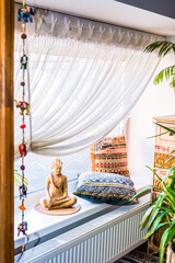 Indian style of interior with buddha boho pillowcases and white curtains