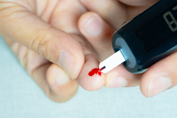 A man draws blood and checks for diabetes and high blood sugar levels with a digital blood sugar...