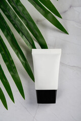 Plastic tube for cream or lotion. Skin care or sunscreen cosmetic with stylish props on tropical...