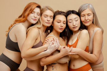 Group of attractive cheerful multiracial women wearing stylish lingerie embracing with closed eyes
