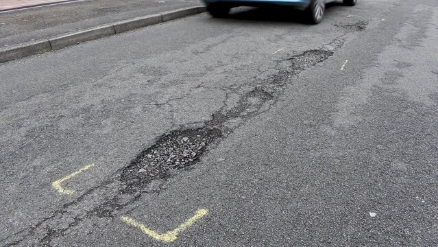 Potholes in the centre of a residential road in the United Kingdom. Cars having to drive close to the kerb to avoid them