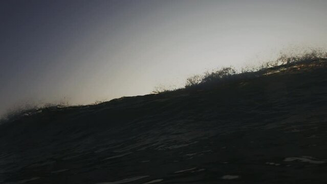 Frontal view of wave breaking and crashing down spreading mist and green sunset light across water