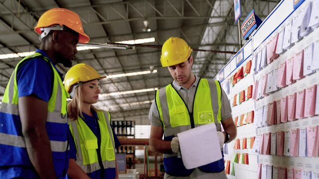 A warehouse worker matures logistics manager talking with a team of dispatchers in a meeting. Group of warehouse employees using a digital warehouse management system.