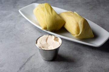 A view of a condiment cup of butter spread next to a plate of Salvadoran corn tamales.