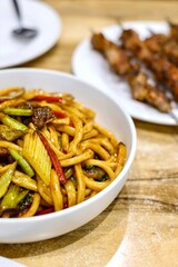 Goshilik lagman, a Uyghur dish of fresh handmade noodles stir-fried with meat and vegetables with a plate of grilled cumin lamb skewers at Apandim Xinjiang Restaurant in Burwood Chinatown, Sydney, NSW