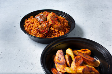 A view of a container of beef stew jollof rice, with a side of roasted plantains.
