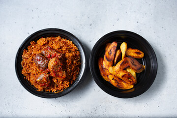 A top down view of a container of beef stew jollof rice, with a side of roasted plantains.