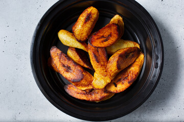 A top down view a black container of sliced roasted plantains.