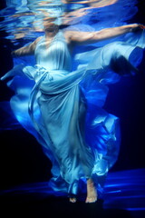 Beautiful girl in a blue dress swims underwater
