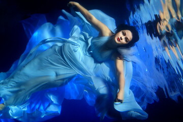 Obraz na płótnie Canvas Beautiful girl in a blue dress swims underwater