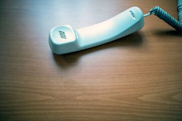 White handset of landline phone on wooden table. Telecomunication concept background