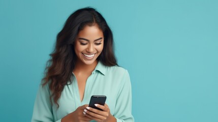 Fototapeta premium Young adult smiling happy pretty latin woman holding mobile phone looking at smartphone, typing message doing ecommerce shopping on cell, using trendy apps on cellphone isolated on blue background