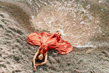 Woman red dress sea. Female dancer in a long red dress posing on a beach with rocks on sunny day