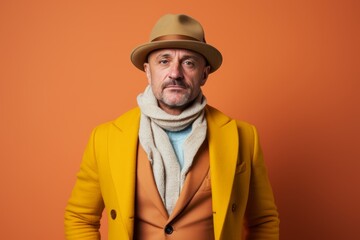 Senior man in yellow coat, hat and scarf. Studio shot.