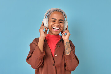 Young laughing African American woman presses wireless headphones to ears listening to audio...