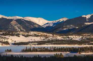 Beautiful view Colorado mountain range with frozen lake in foreground lit by setting sun