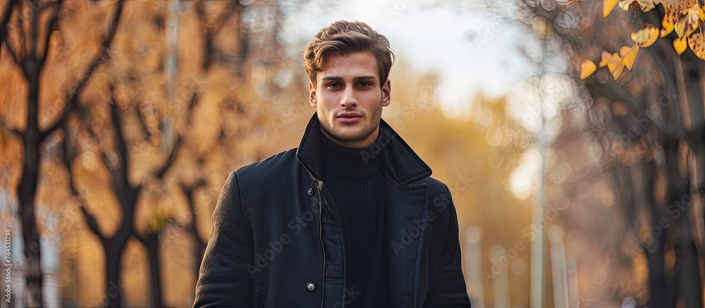 Poster An attentive gentleman dressed in a black coat and turtleneck sweater is standing in a park