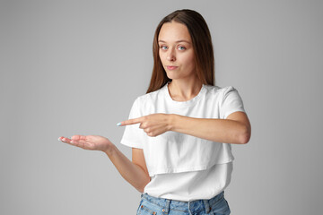 Young woman wearing casual outfit pointing empty space on gray background