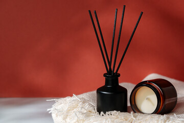 Aromatic Reed Diffuser and Scented Candle on a Woven Mat Against a Warm Red Background