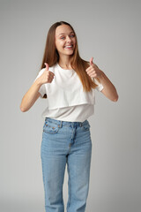 Smiling young woman showing thumbs up sign on gray background