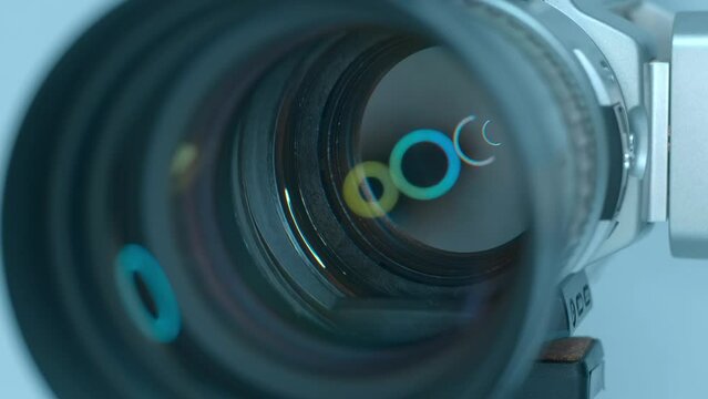 In the studio, ring LED light is reflected in a powerful zoom lens of a professional video camera standing on a tripod against a light background. Closeup. Macro. Shot in motion