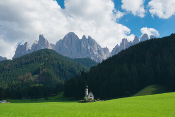 Fototapeta na wymiar View of the Church of St. Johann is in a beautiful scenic location against the Geisler peaks covered with clouds in Santa Maddalena village, Val Di Funes, Italy