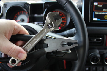 The driver holds in his hand set of tools for repair in front of the blurred tachometer in vehicle...