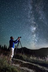 Professional photographer taking photos of Milky Way. Young male focusing his camera to take...