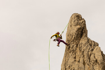 A man is climbing a rock with a green rope. Concept of adventure and excitement, as the man is...