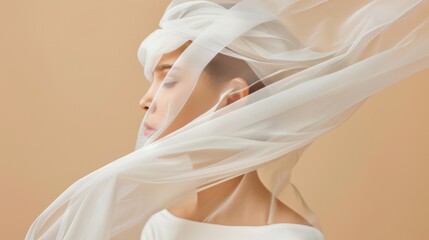 Fototapeta na wymiar Beautiful young woman wrapped in transparent fabric. Fluttering veil on a beige background