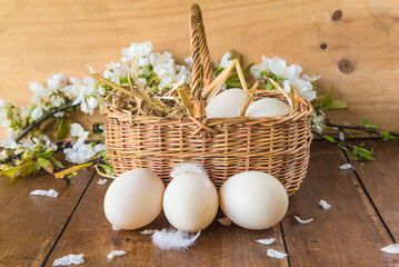 Easter holiday greeting card: wicker basket with hen's eggs and apple blossom on a wooden background
