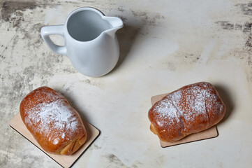 Homemade buns with jam with powdered sugar on wooden background. Fresh bakery and milk jug on kitchen table. Sweet breakfast