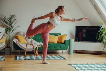 Smiling woman in sportswear is practicing a yoga pose in a living room. Healty life concept