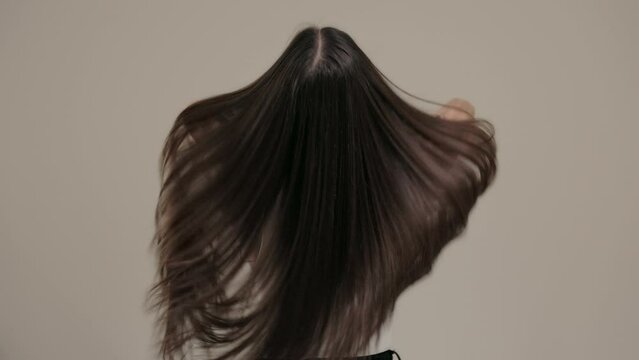 Brunette girl with long straight hair, rear view in the studio on a light background.