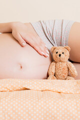 Closeup of pregnant woman with teddy bear lying on bed