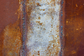 Close up of a brownish rusted welded sheet metal surface with yellowish and orange hue and amber patina.